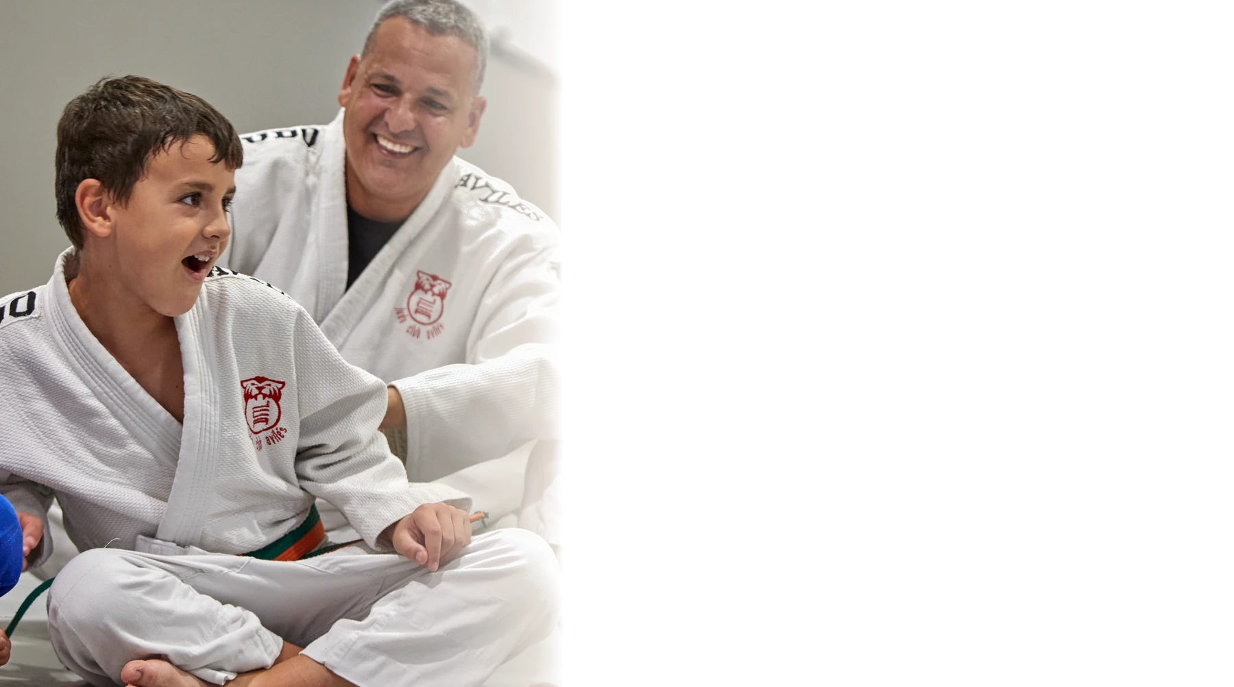 Un niño sonríe junto a su entrenador sentados en el tatami.