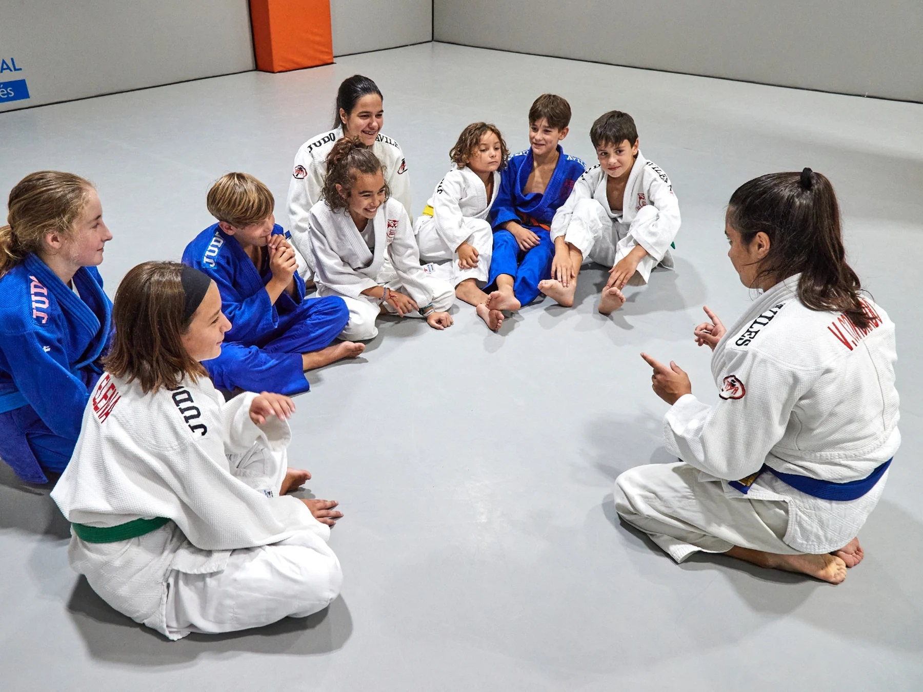 Un grupo de judocas sentados en círculo escuchando a su entrenadora.